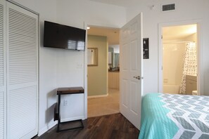 Habitación de hotel con una cama, un televisor montado en la pared, una mesita y una puerta que da a un baño.