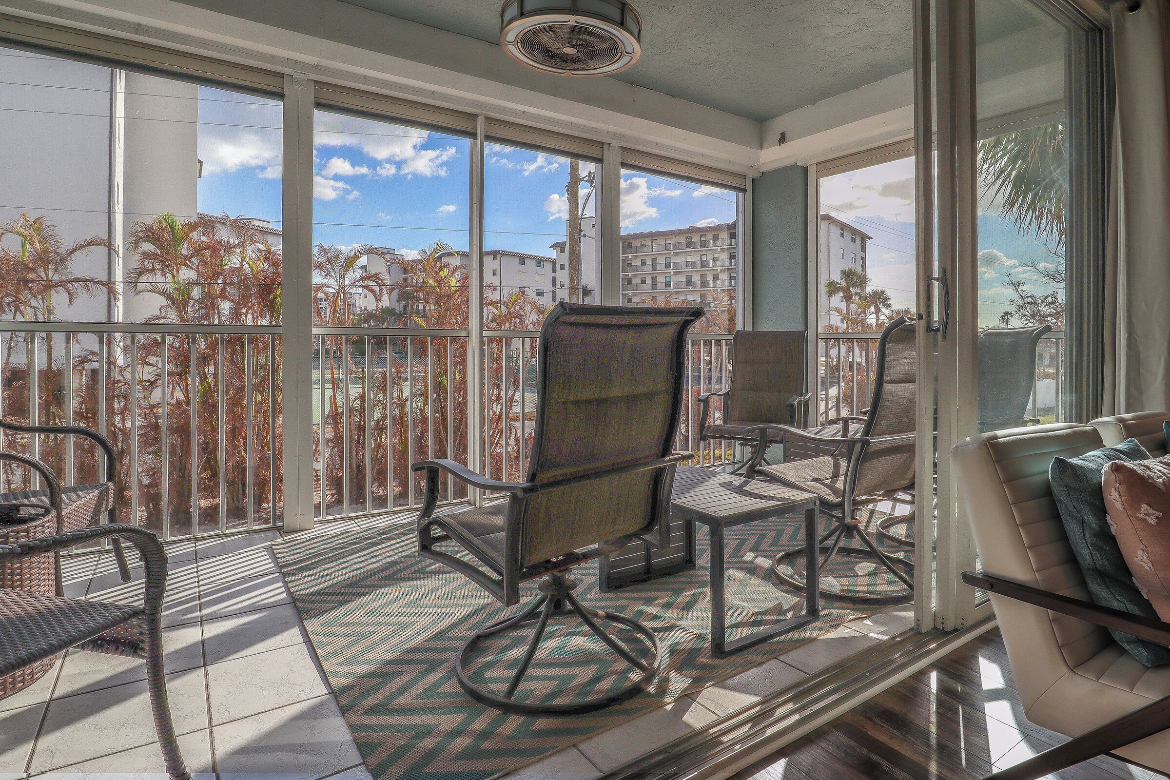 A balcony with a view of palm trees and buildings, furnished with chairs and a table.