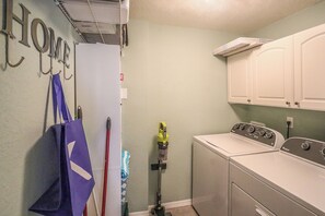 Una sala de lavandería con lavadora, secadora y un estante con productos de limpieza.