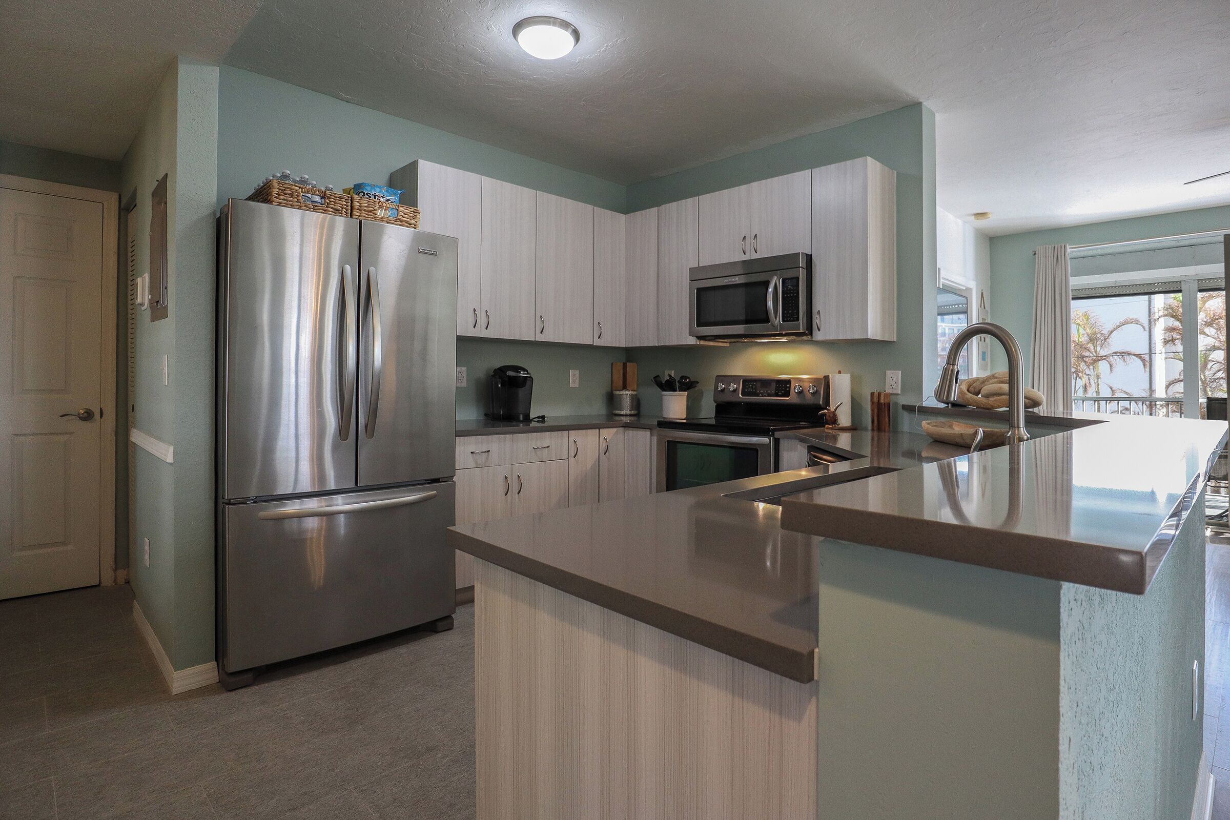 A modern kitchen with stainless steel appliances, light wood cabinets, and a large island with a sink.