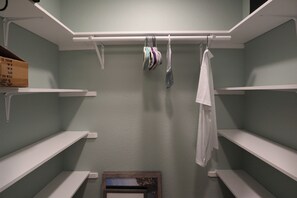 Un armario con estantes blancos y espacio para colgar, una caja a la izquierda y un espejo pequeño en la parte inferior.