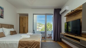 Ein modernes Hotelzimmer mit einem großen Bett, einem Flachbildfernseher, einem Balkon mit Stadtblick und einem hölzernen Kleiderschrank.