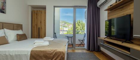 Una habitación de hotel moderna con una cama grande, un televisor de pantalla plana, un balcón con vistas a la ciudad y un armario de madera.