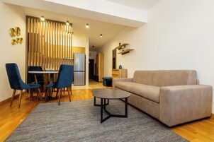 Un salon moderne avec un canapé, deux fauteuils, une petite table et un coin cuisine à l’arrière-plan.