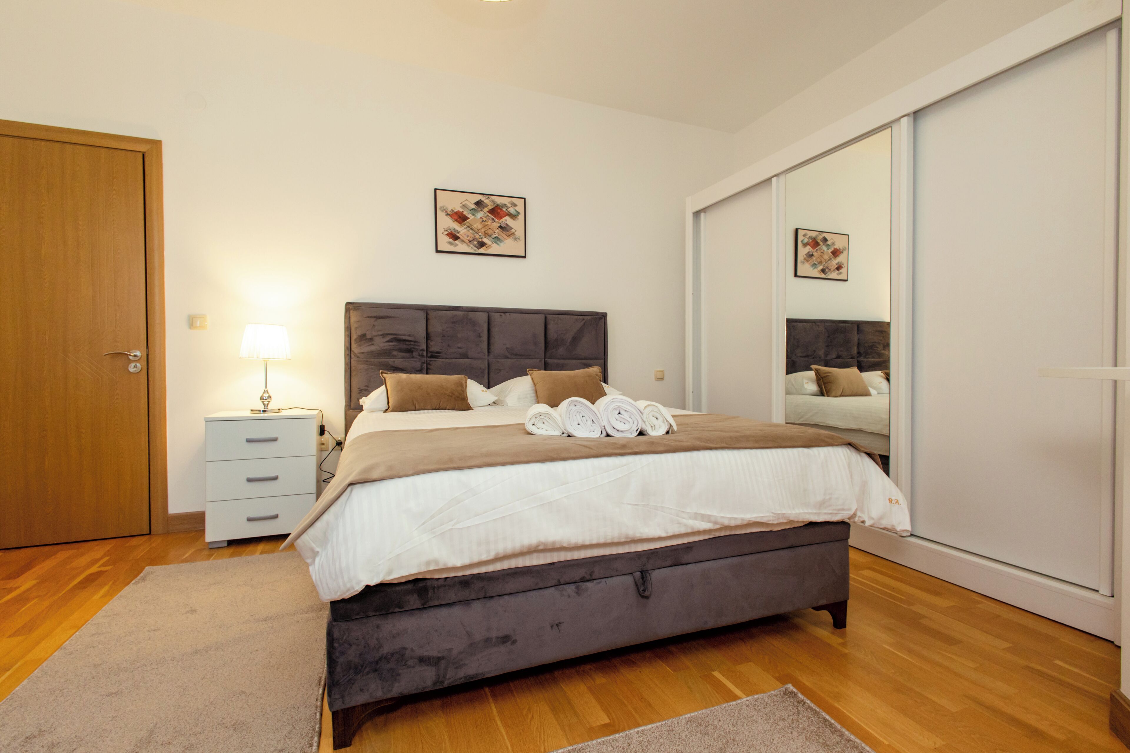 Une chambre à coucher avec un grand lit, une table de chevet, une lampe, un miroir et une armoire.
