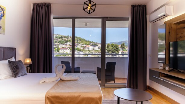 Ein Hotelzimmer mit einem großen Bett, einem Flachbildfernseher, einem Balkon mit Blick auf die Stadtlandschaft und einem Essbereich.