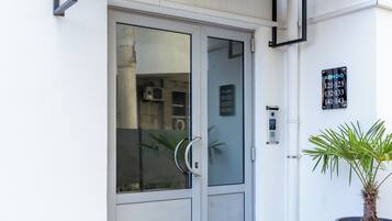 Une entrée moderne avec une porte en verre, un pot de fleurs et un panneau indiquant les numéros des appartements.