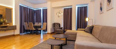 A modern living room with a sofa, two armchairs, a coffee table, and a dining area with a table and chairs.