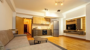 Ein modernes Wohnzimmer mit einer Couch, einem Couchtisch und einer Küchenzeile mit Holzausstattung und einem Kühlschrank.