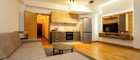 A modern living room with a sofa, a coffee table, and a kitchen area with wooden cabinets and a refrigerator.