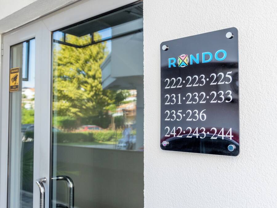 Ein schwarzes Schild mit dem Namen "RONDO" und einer Liste von Telefonnummern an einer weißen Wand.