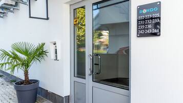 Una entrada moderna de edificio con puerta de vidrio, planta en maceta y cartel con números de teléfono.