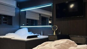 Une chambre d’hôtel moderne dotée d’un grand lit, d’une salle de bain avec baignoire, d’un miroir et d’un téléviseur à écran plat fixé au mur.