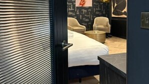 Une chambre à coucher moderne avec un lit, deux fauteuils, une table basse et des œuvres d’art accrochées au mur.