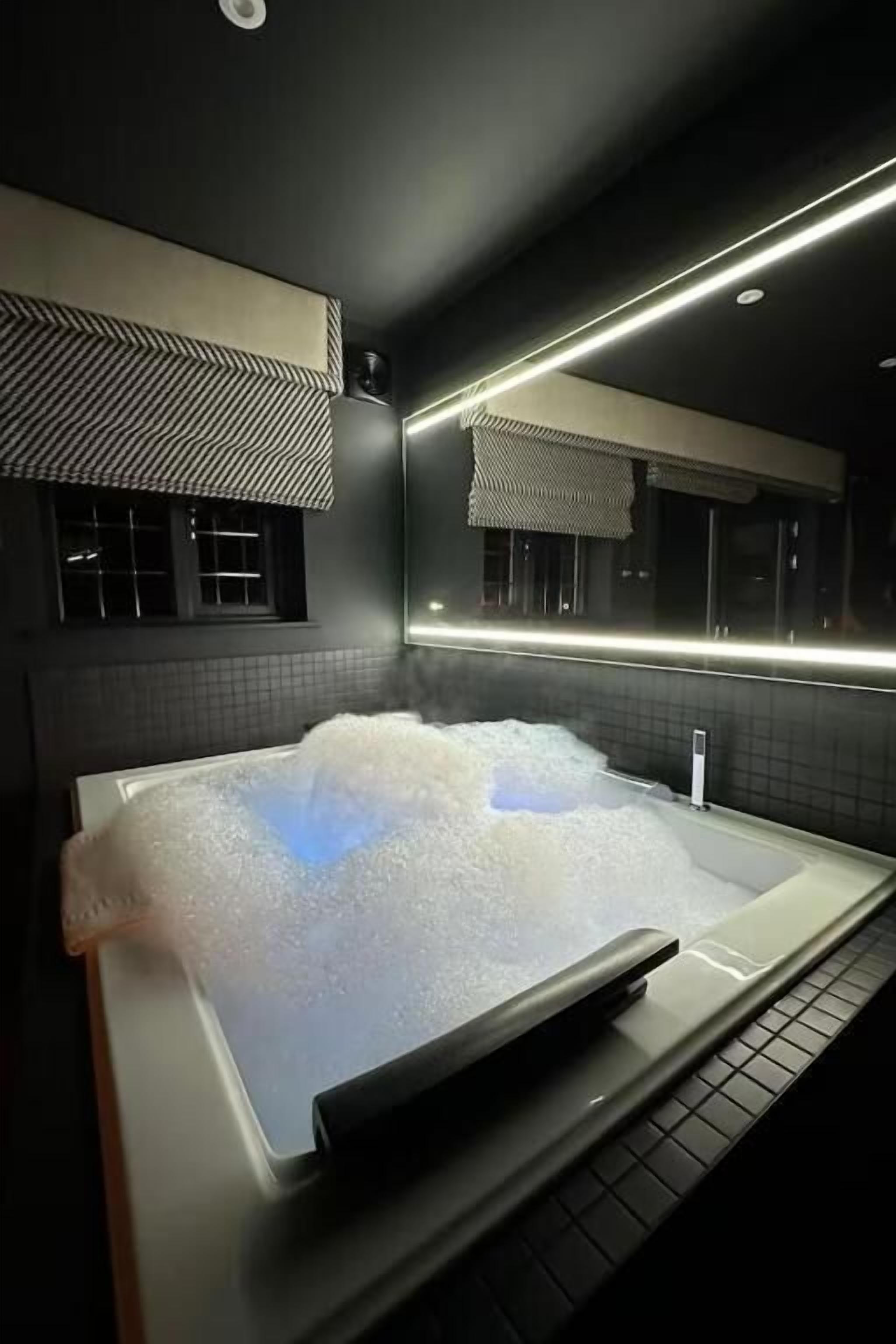 A modern spa room with a large hot tub, a window with a view, and a ceiling with recessed lighting.