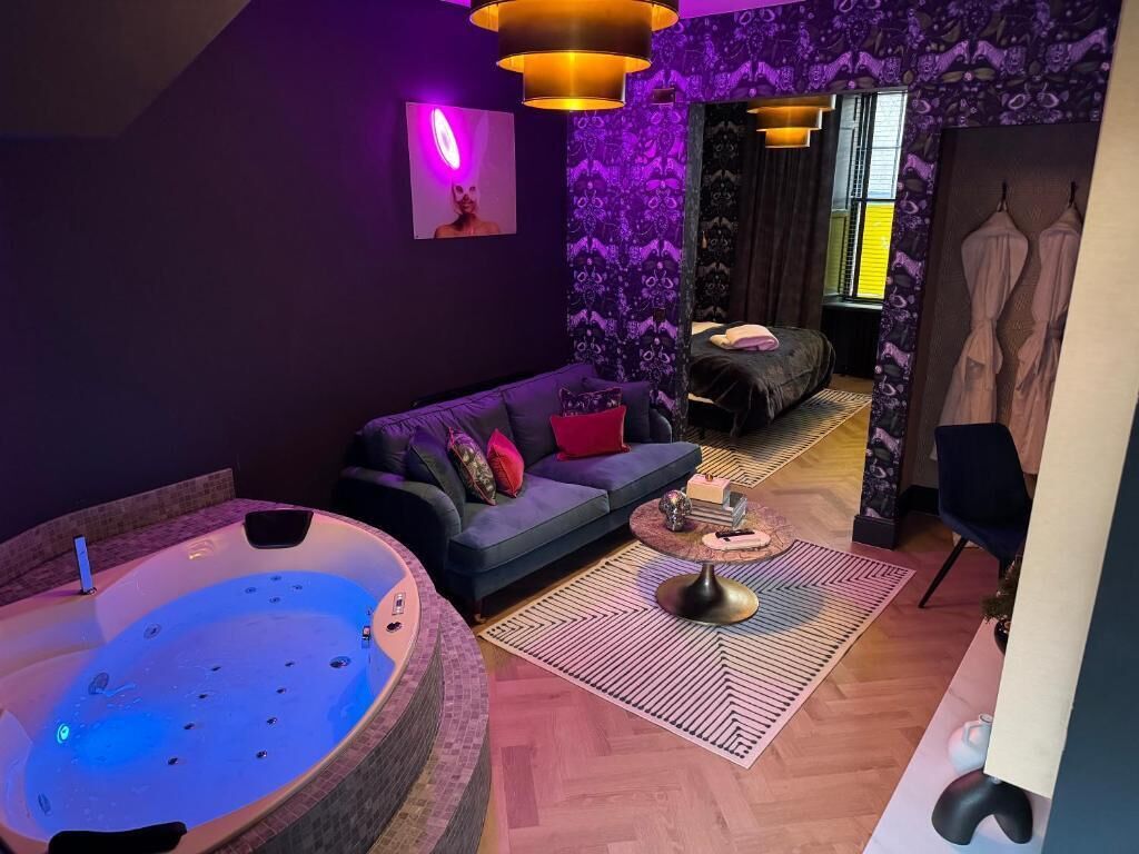 Un spa moderno con un jacuzzi grande, un sofá oscuro y una pared con estampado.