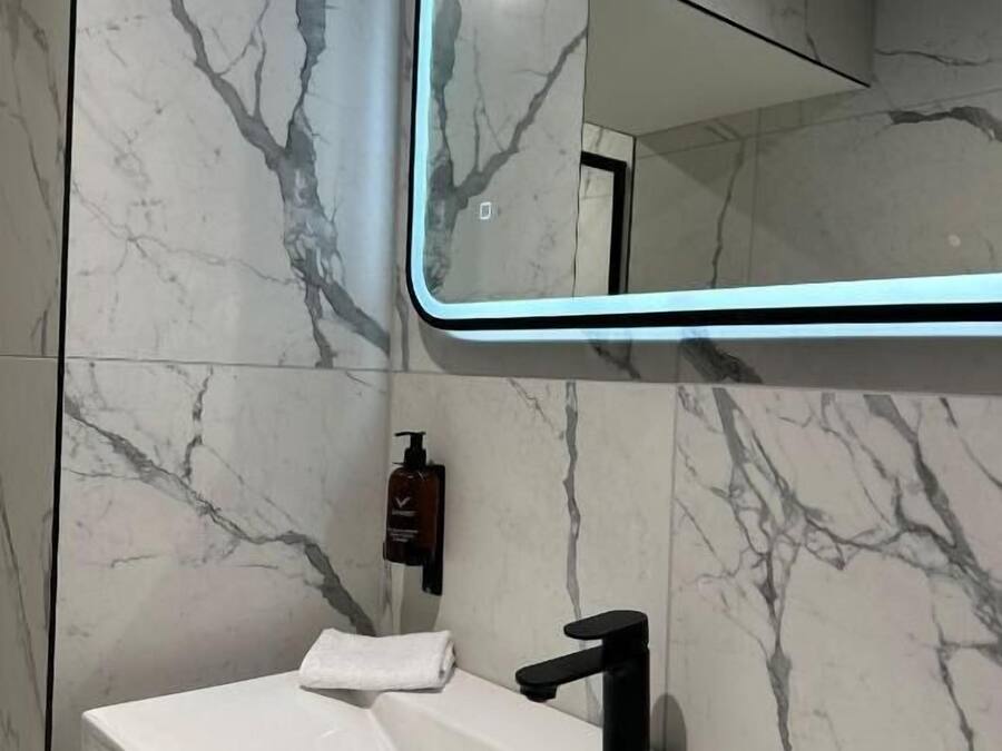 A bathroom with a white sink, black faucet, and a mirror with a neon light frame.