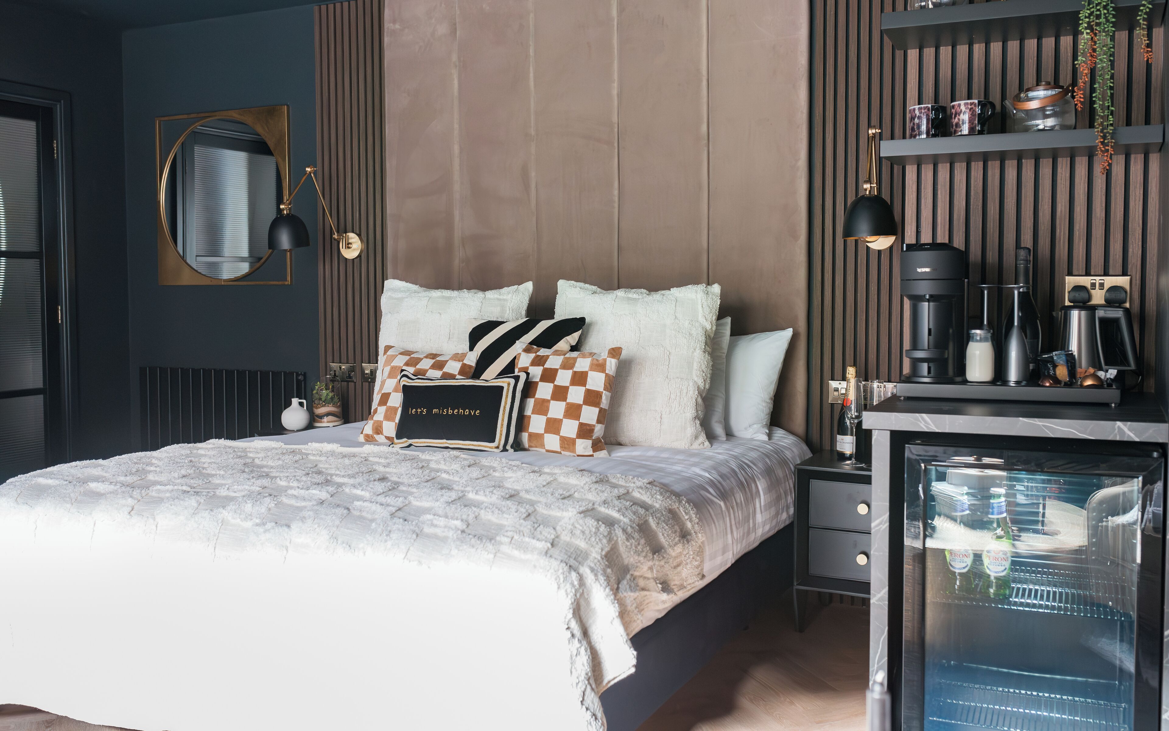 A modern bedroom with a bed, bedside tables, a mirror, and a coffee machine.