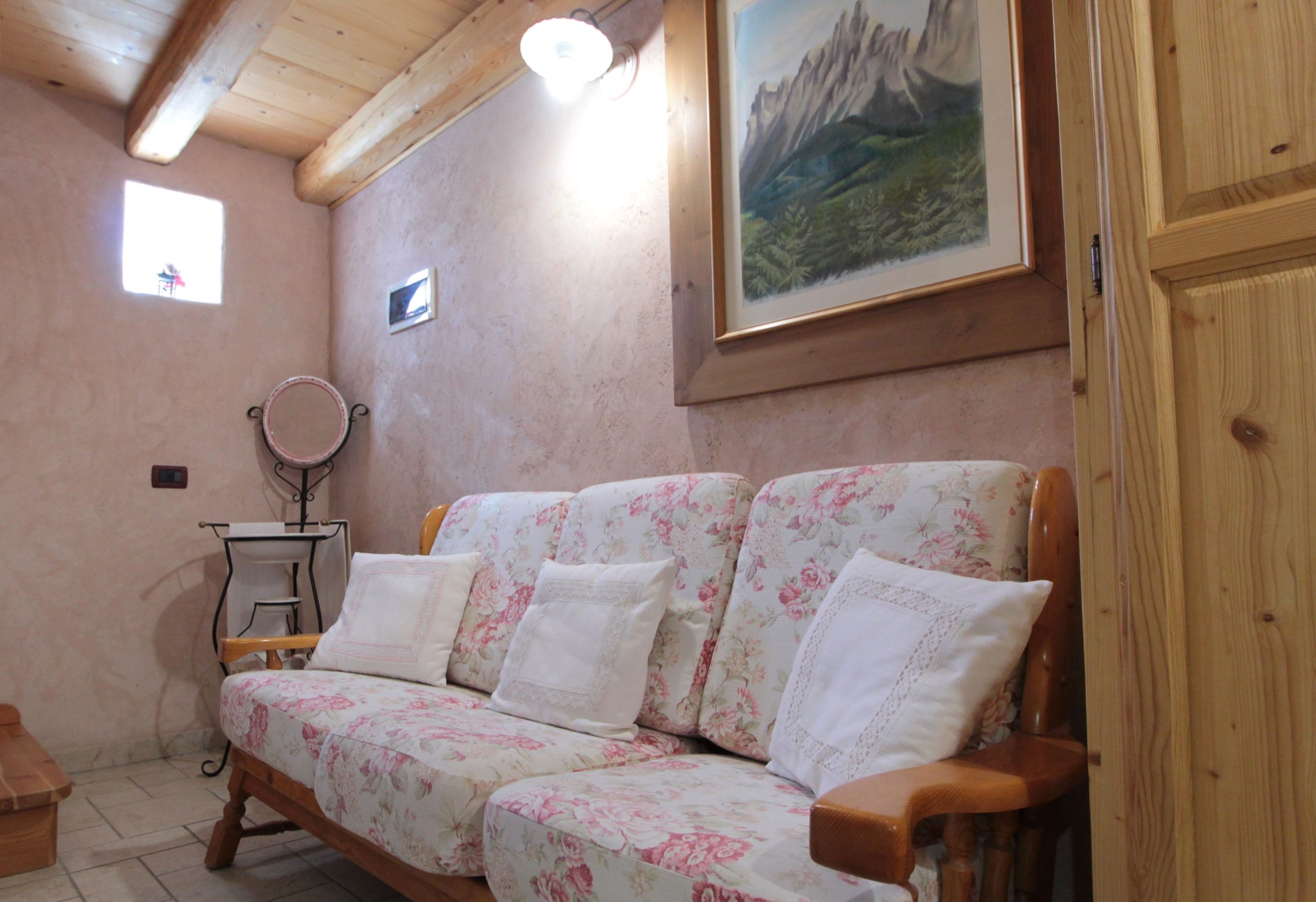 Um quarto aconchegante com um sofá floral, uma mesinha, um espelho e um quadro pendurado na parede.