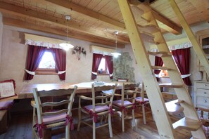 A wooden dining area with a table and chairs, a stone wall, and a wooden staircase. - Baita Mountain View Pale San Martino (Primiero San Martino di Castrozza)
