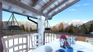 A table set outdoors with a mountain view, wooden chairs, and a hanging light fixture.