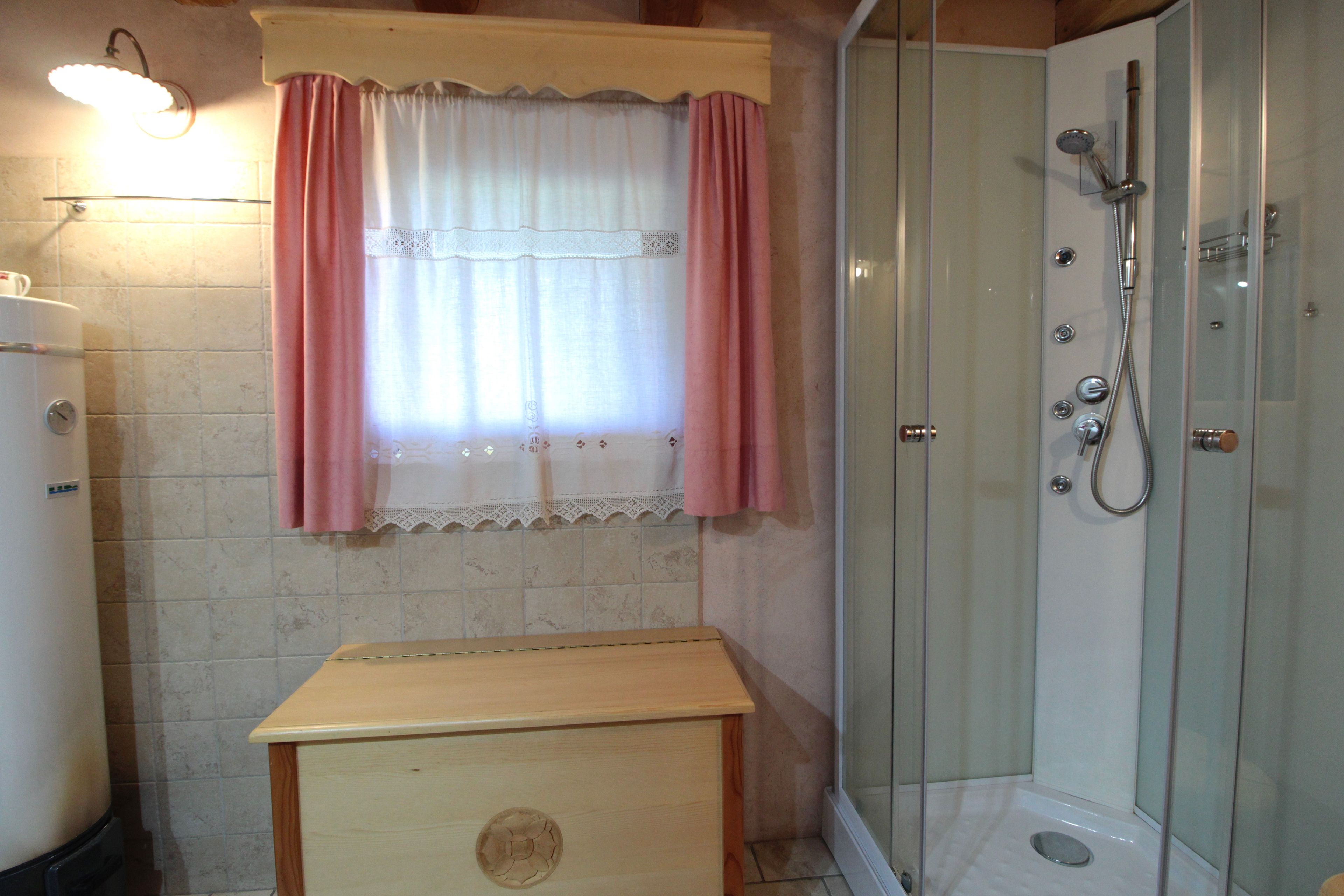 Een badkamer met een douche, een houten kastje en een raam met gordijnen.