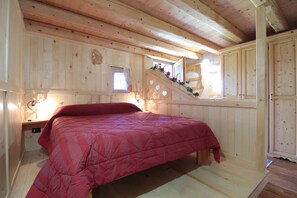 Un interior de madera con una cama, un ventanal pequeño y una escalera.