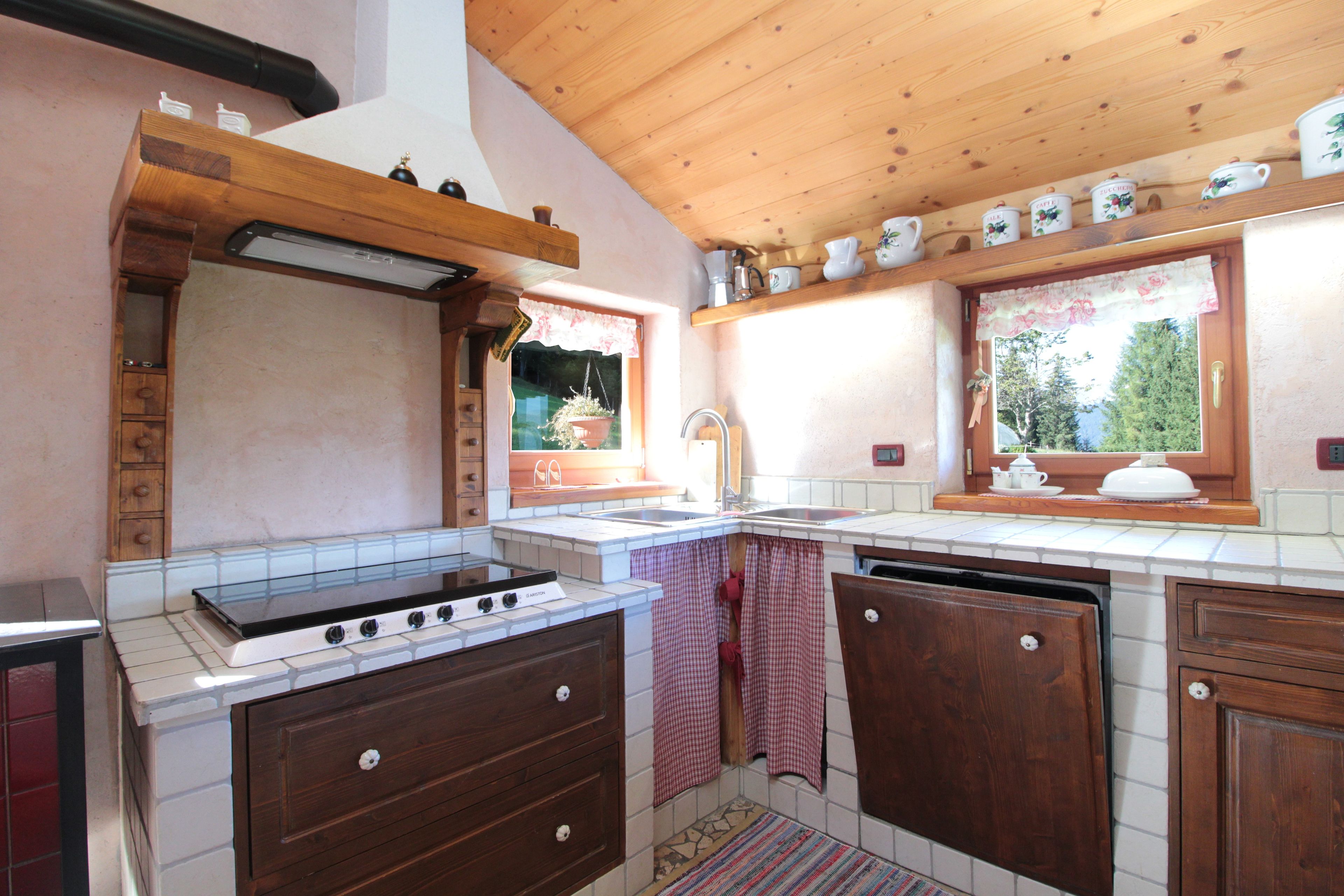 A kitchen with a stove, sink, wooden cabinets, and a window with a view of greenery.