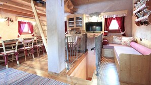 A wooden interior with a loft bed, a television, and a dining area with chairs and a table.