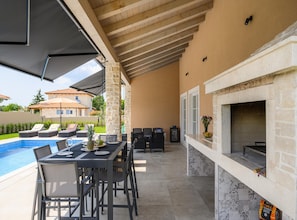 Patio esterno con piscina, tavolo da pranzo, sedie e zona barbecue.