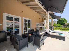 Une terrasse extérieure aménagée avec des meubles en osier, un barbecue et une piscine.