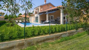 Une maison à deux étages dotée d’une piscine, d’un patio couvert et de piliers en pierre.