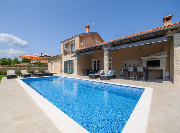 Une piscine avec des chaises longues et un espace barbecue.