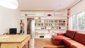 A living room with a wooden table, a red leather sofa, and a white bookshelf filled with books. - Elegant apartment in Trastevere- Bolognese 45 (Rome)