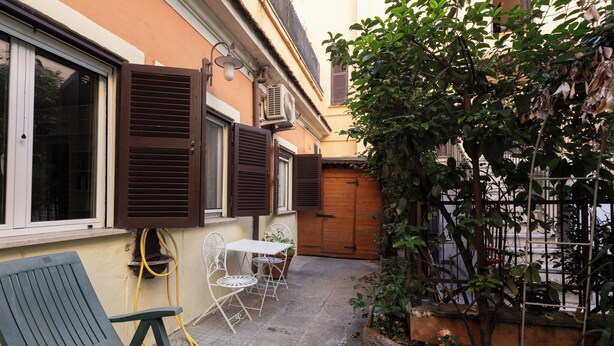 A courtyard with a table and chairs, a bench, a wooden door, and a small garden area. - Elegant apartment in Trastevere- Bolognese 45 (Rome)