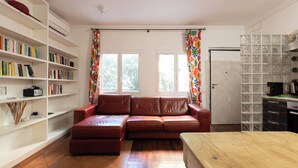 A living room with a leather sofa, a wooden table, a bookshelf, and a kitchen area with a refrigerator and a tiled backsplash. - Elegant apartment in Trastevere- Bolognese 45 (Rome)