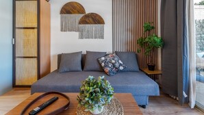 Ein modernes Wohnzimmer mit einer Couch, Fernbedienungen, einer Zimmerpflanze und einem an der Wand befestigten Regal.
