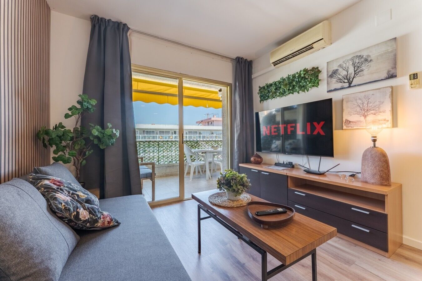 Een moderne woonkamer met een bank, een salontafel, een televisie en een balkon met een gele parasol.