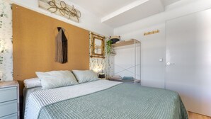Ein Schlafzimmer mit einem Bett, einem Nachttisch, einem Kleiderschrank, einem Spiegel und einer hängenden Pflanze.