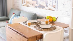 A dining area with a table set for two, a bowl of fruit, and a window with a view of rocks. - Salou Luxe Stay | Chill-out | Cozy ( 2BR ) Parking (Salou)