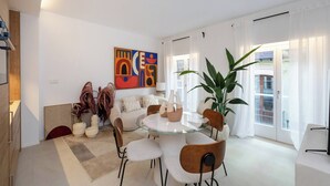 Una sala de estar moderna con una mesa redonda de vidrio, asientos cómodos, una planta grande en maceta y un cuadro abstracto colorido en la pared.