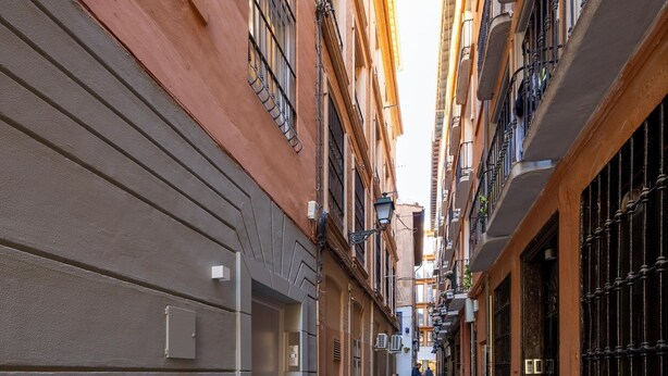 A narrow urban street flanked by buildings with balconies and windows.