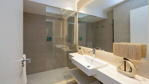 Un baño moderno con ducha de vidrio, dos lavamanos y un espejo grande.