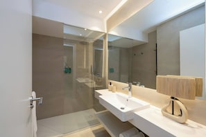 Un baño moderno con ducha de vidrio, dos lavamanos y un espejo grande.
