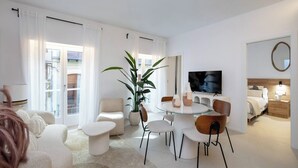 Una sala moderna con una mesa redonda de vidrio, sofás blancos y una planta grande en maceta.