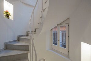 Una escalera con barandilla, una ventana con vistas al exterior y una planta pequeña en la pared.
