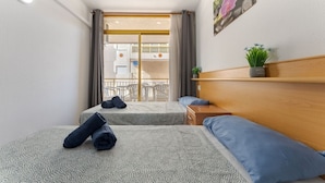 Et hotelværelse med to senge, en træsenggavl, et lille bord, en potteplante og en balkon med udsigt.