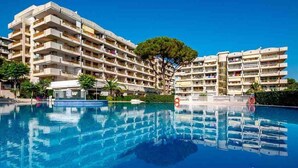 Et hotel med flere etager, altaner, en swimmingpool og et stort træ i baggrunden.