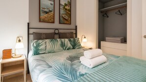 Une chambre à coucher comprenant un lit, deux tableaux accrochés au mur, une table de chevet avec une lampe, une commode et une armoire.
