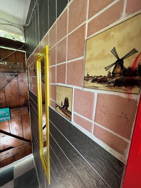 A room with a wooden door, a yellow ladder, and a wall with a windmill painting. - Camping De Helleborus (Groningen)